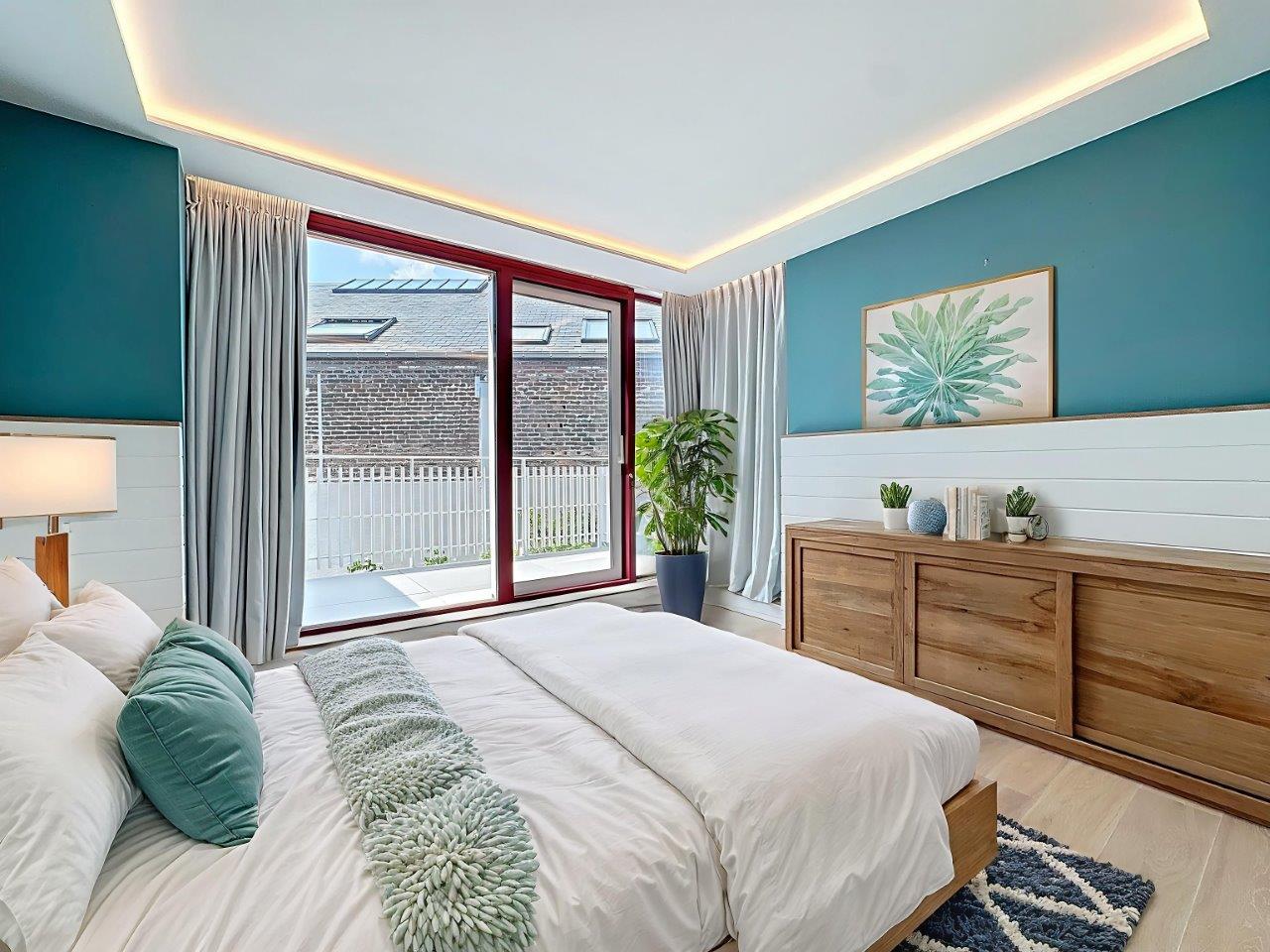 Chambre moderne en teal avec vue sur la nature, mobilier épuré et décor végétal.