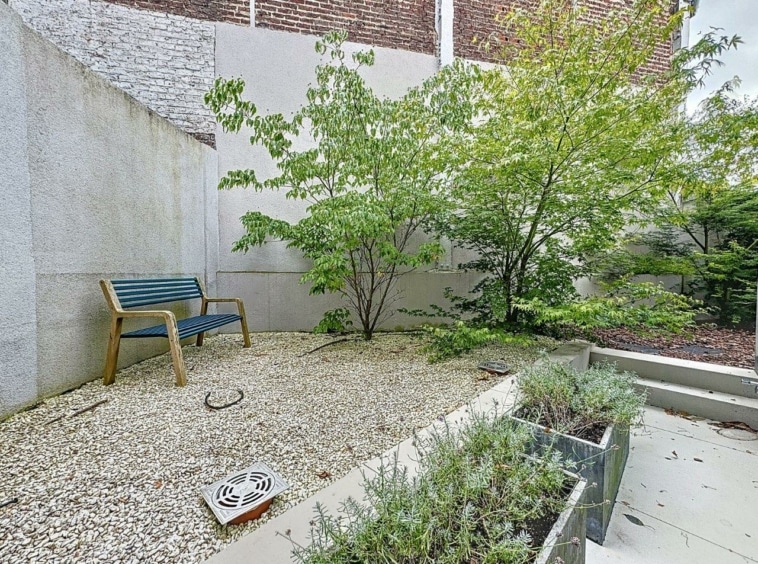 Coin de jardin paisible avec banc en bois bleu, verdure et murs en briques.