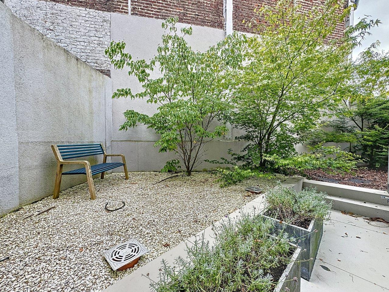 Coin de jardin paisible avec banc en bois bleu, verdure et murs en briques.