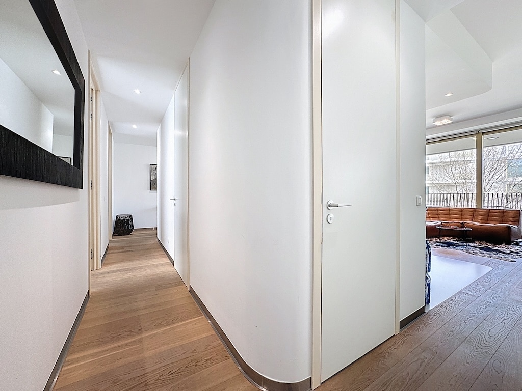 Couloir moderne lumineux avec miroir, portes épurées et vue sur un espace salon chaleureux.