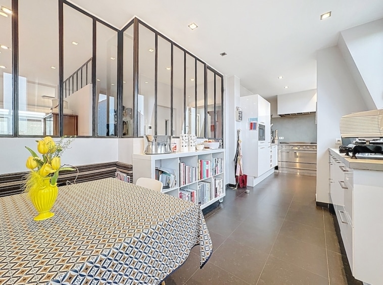 Cuisine moderne lumineuse avec salle à manger ouverte, cloison en verre, mobilier élégant et éclairage naturel.