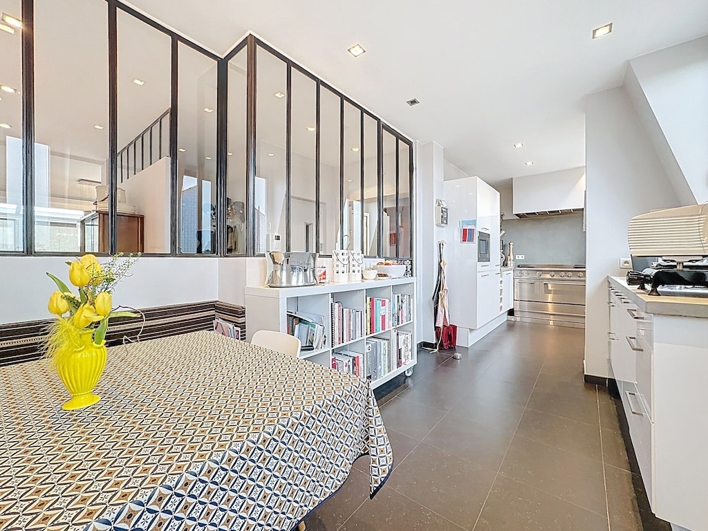 Cuisine moderne lumineuse avec salle à manger ouverte, cloison en verre, mobilier élégant et éclairage naturel.