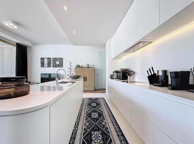 Cuisine moderne blanche avec îlot courbé, tapis coloré et éclairage encastré pour un style contemporain.