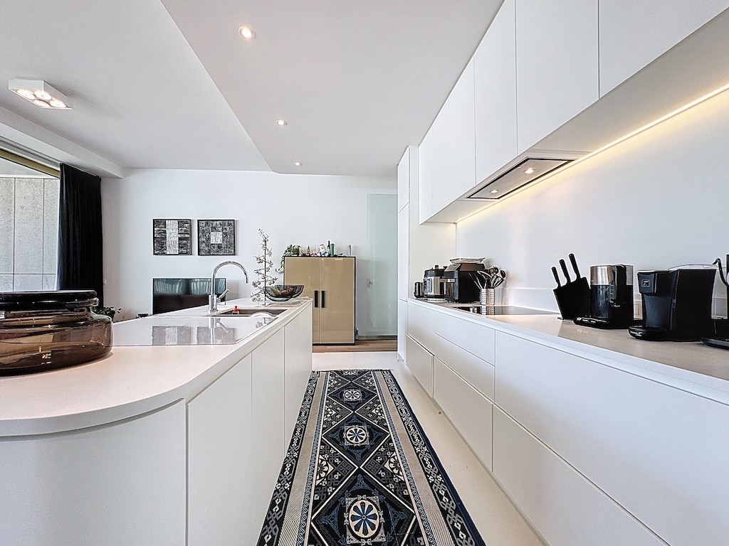 Cuisine moderne blanche avec îlot courbé, tapis coloré et éclairage encastré pour un style contemporain.
