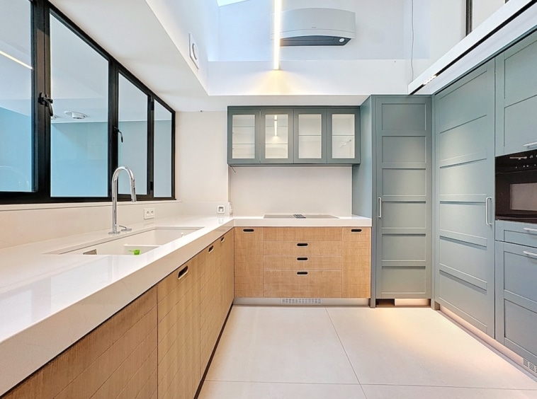 Cuisine moderne avec meubles en bois clair, bleu-vert, grande luminosité naturelle et design élégant.