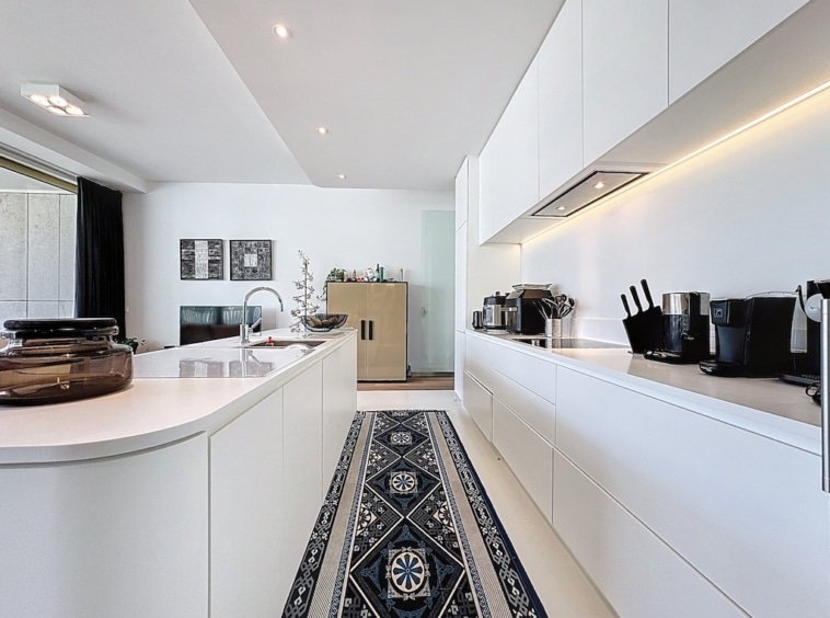 Cuisine moderne blanche, éclairage chaleureux, tapis bleu et blanc, ambiance fonctionnelle et cosy.