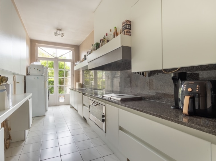 Cuisine moderne lumineuse avec armoires blanches, plan en granite et électroménagers élégants.