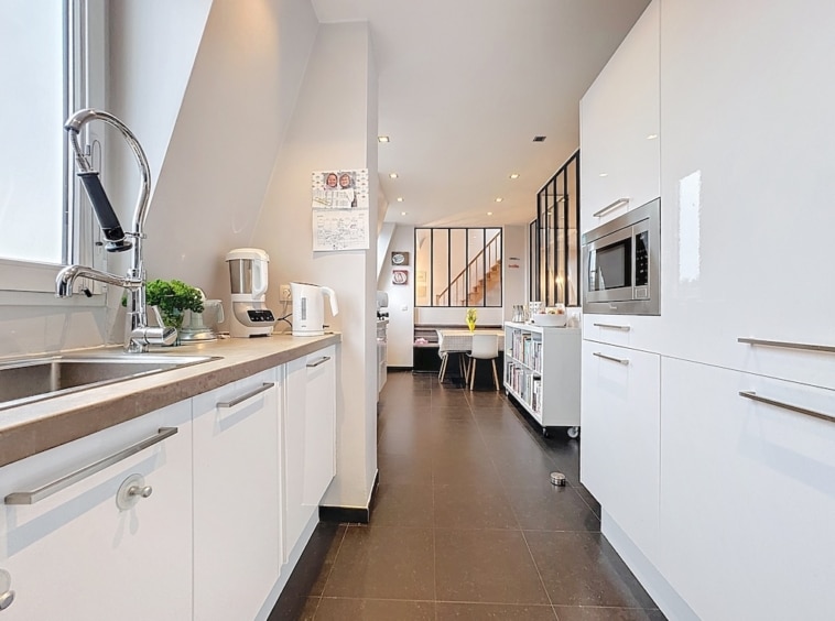 Cuisine moderne lumineuse avec meubles blancs, plan épuré, espace ouvert et luminosité naturelle.