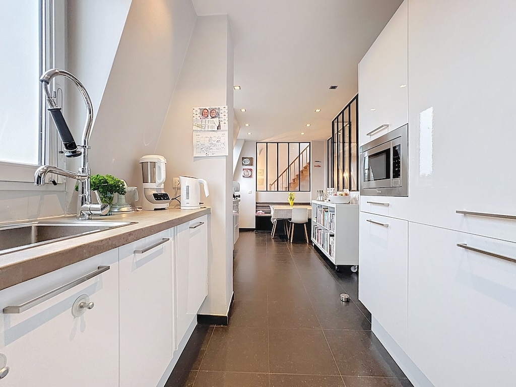 Cuisine moderne lumineuse avec meubles blancs, plan épuré, espace ouvert et luminosité naturelle.