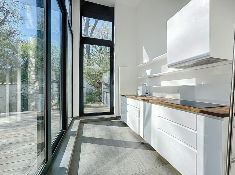 Cuisine moderne lumineuse avec vue sur jardin, bois chaleureux, design épuré, espace convivial et naturel.