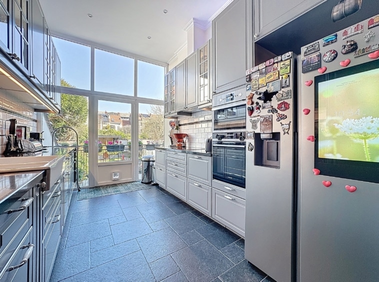 Cuisine moderne lumineuse avec grandes fenêtres, électroménagers intégrés et sol en carrelage foncé.