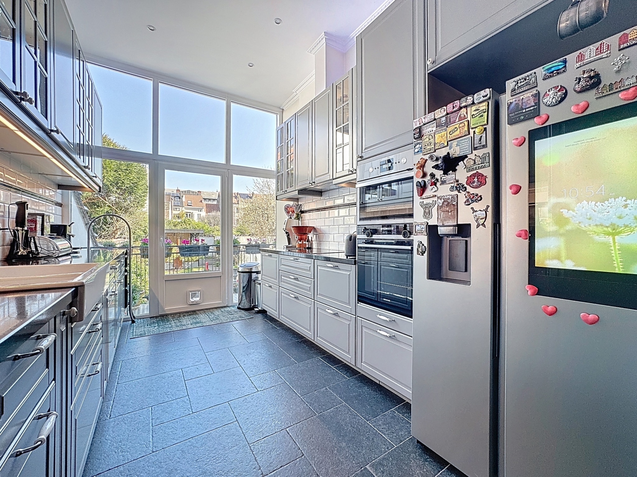 Cuisine moderne lumineuse avec grandes fenêtres, électroménagers intégrés et sol en carrelage foncé.