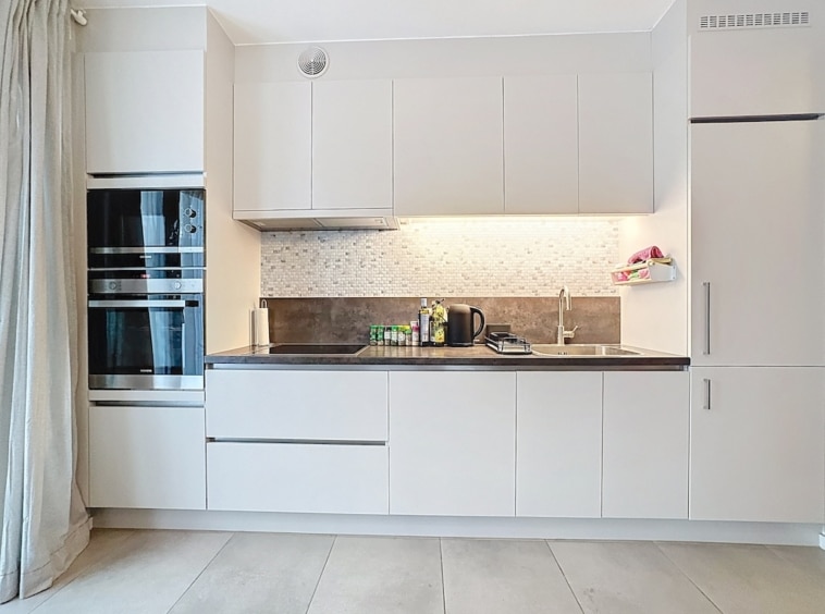 Cuisine moderne minimaliste avec meubles blancs, plan en granit foncé et éclairage sous-meubles.