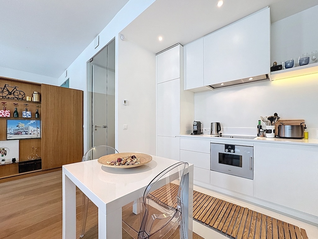 Cuisine moderne minimaliste avec dinette élégante, mobilier blanc, accents en bois et éclairage chaleureux.