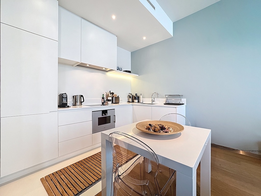 Cuisine moderne minimaliste avec mobilier blanc, électroménagers en acier, sol en bois chaud et murs bleus.