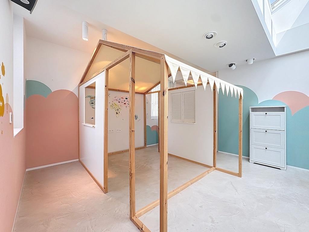 Espace créatif pour enfants avec maison en bois, décor pastel, lumière naturelle et rangement moderne.