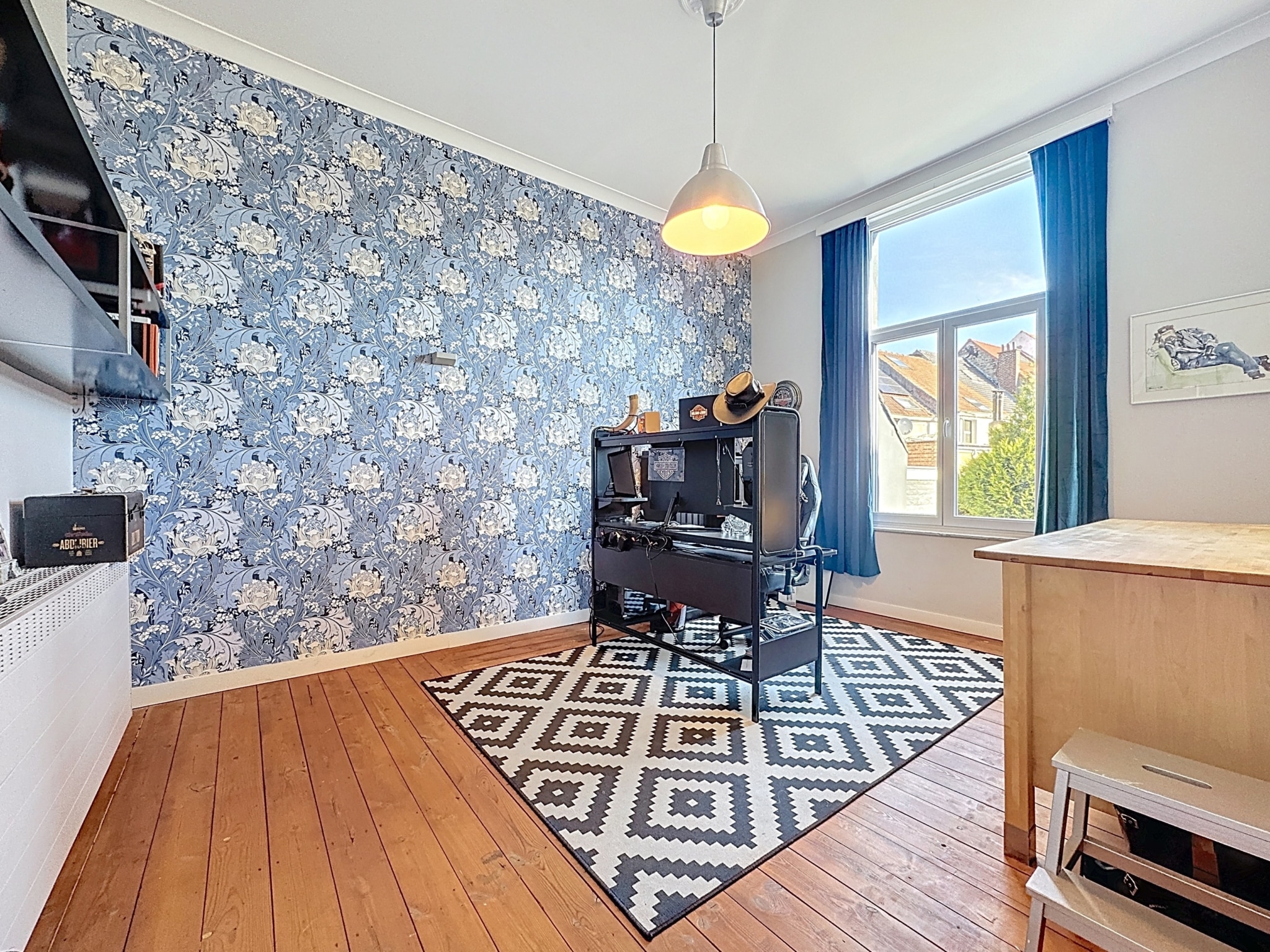 Espace de bureau moderne, lumineux et cosy avec papier peint floral bleu, mobilier minimaliste et tapis géométrique.