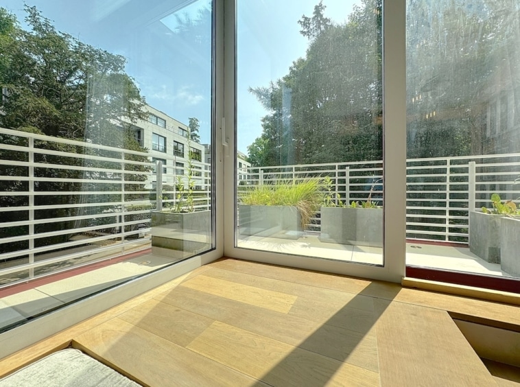 Vue intérieure lumineuse avec patio moderne et verdure, bois chaleureux, ambiance calme et élégante.