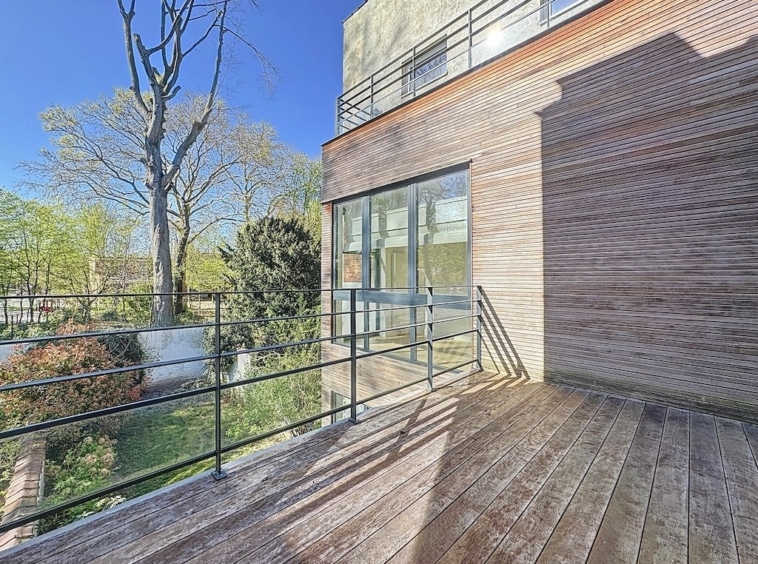 Espace moderne avec deck en bois, façade en briques rouges et jardin apaisant sous ciel bleu.