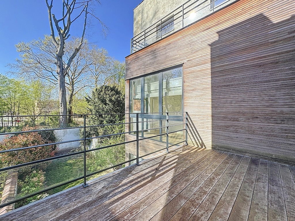 Espace moderne avec deck en bois, façade en briques rouges et jardin apaisant sous ciel bleu.