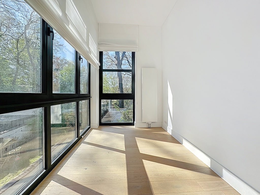 Intérieur moderne minimaliste lumineux avec grandes fenêtres, vue sur la verdure et espace zen.