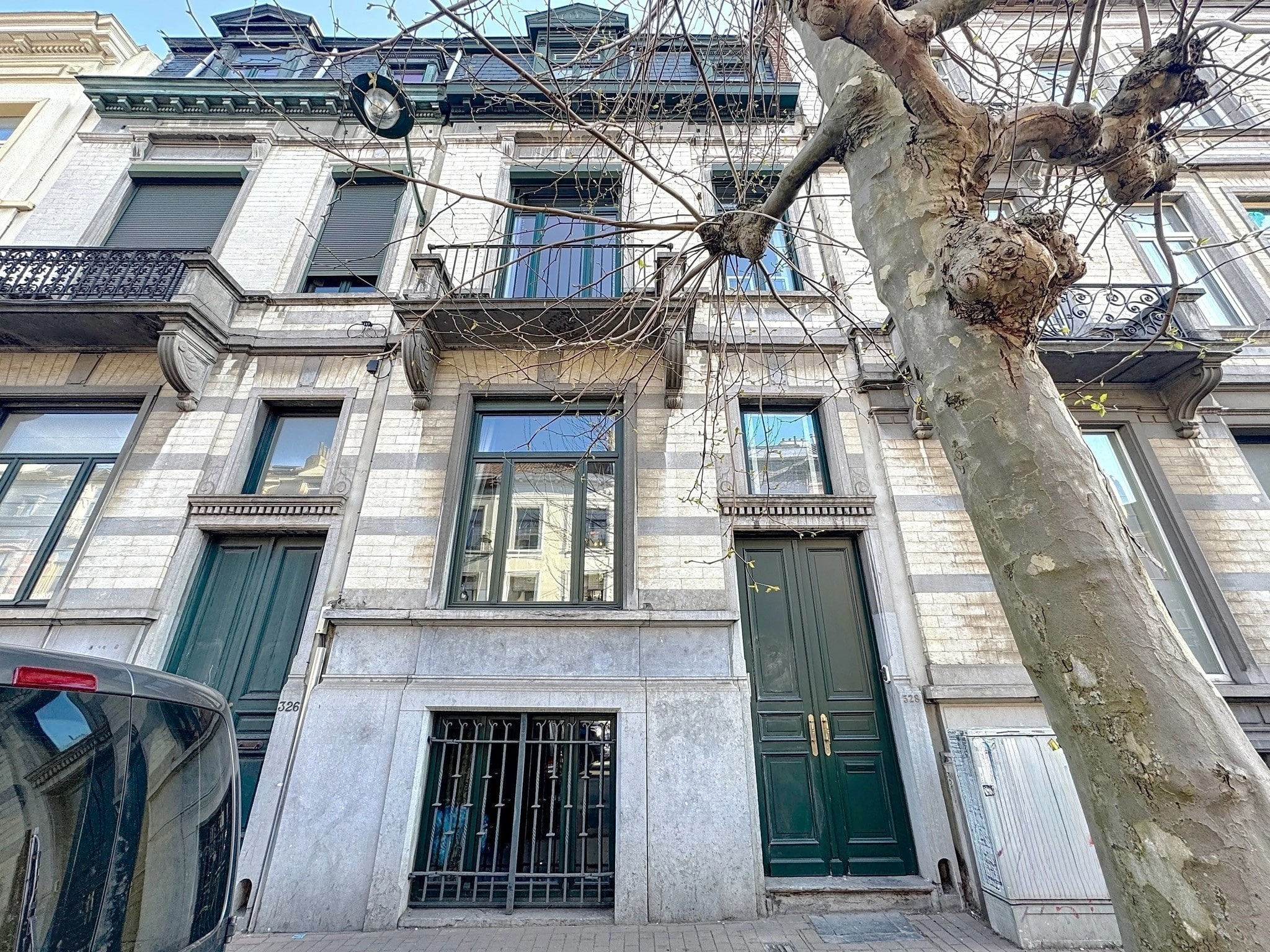Façade élégante à Waterloo avec balcons en fer forgé, fenêtres ornementées et arbre nu en premier plan.