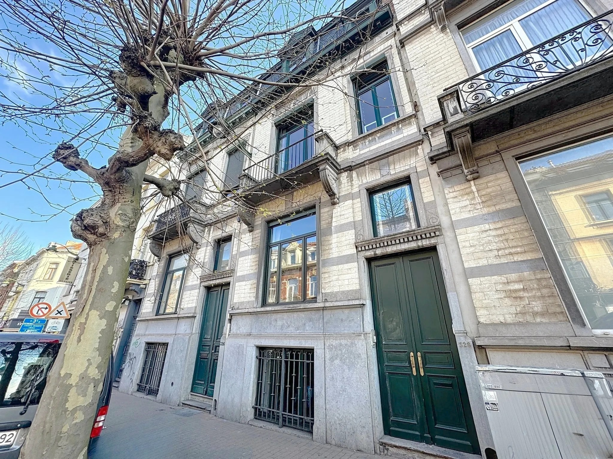 Façade élégante d’un bâtiment historique avec fenêtres symétriques et portes vertes, en centre urbain.