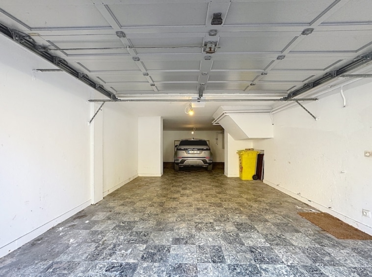 Garage moderne lumineux avec véhicule élégant, sol en carrelage gris, espace propre et organisé.