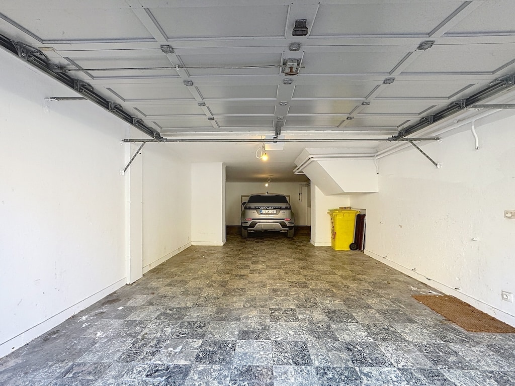 Garage moderne lumineux avec véhicule élégant, sol en carrelage gris, espace propre et organisé.