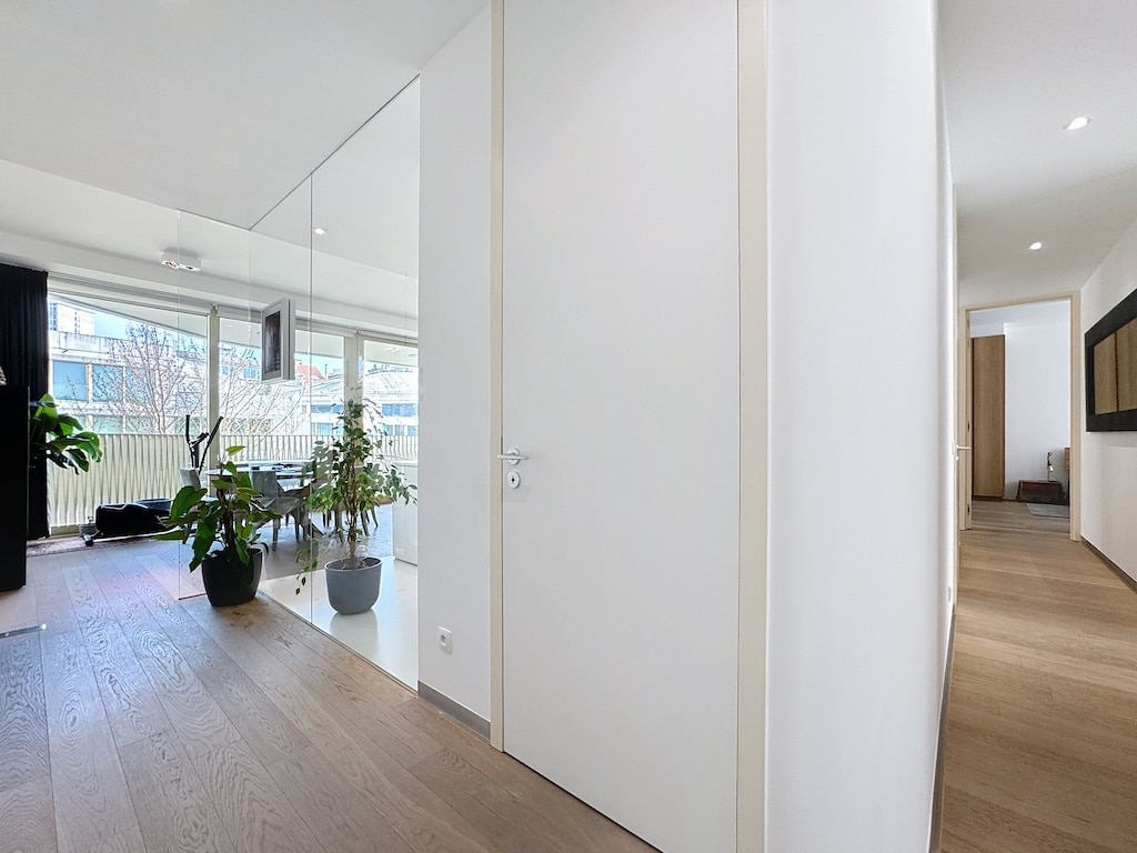 Hall lumineux moderne avec porte blanche, plantes, bois clair et espace de vie convivial.