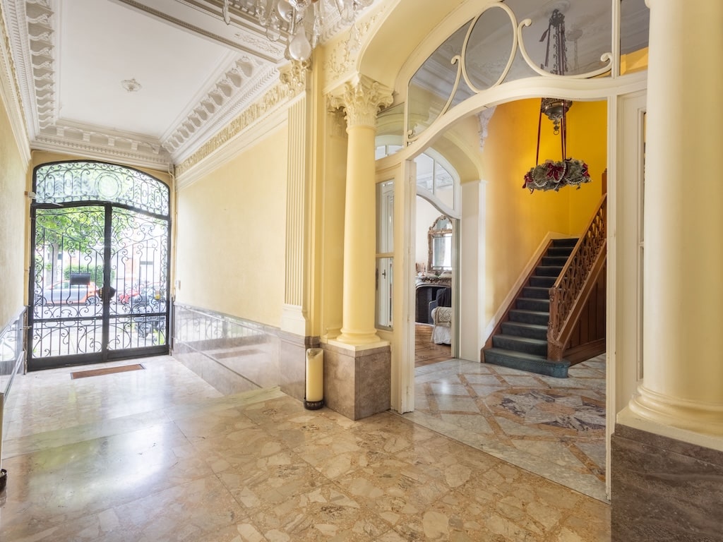 Entrée sophistiquée avec plafond mouluré, escalier en bois et chandelier élégant.