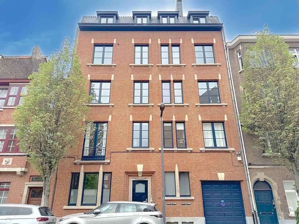 Immeuble moderne en brique rouge avec porte bleue, fenêtres élégantes et arbres en ville.