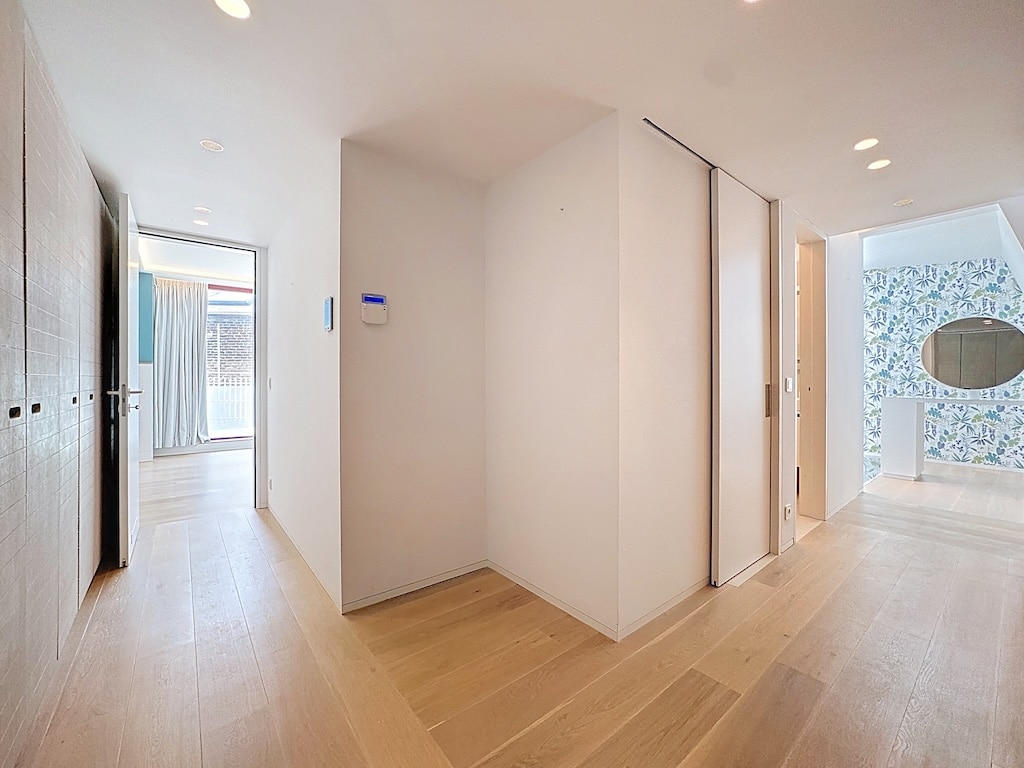 Hall lumineux moderne avec murs blancs, plancher en bois clair et mur floral décoratif.
