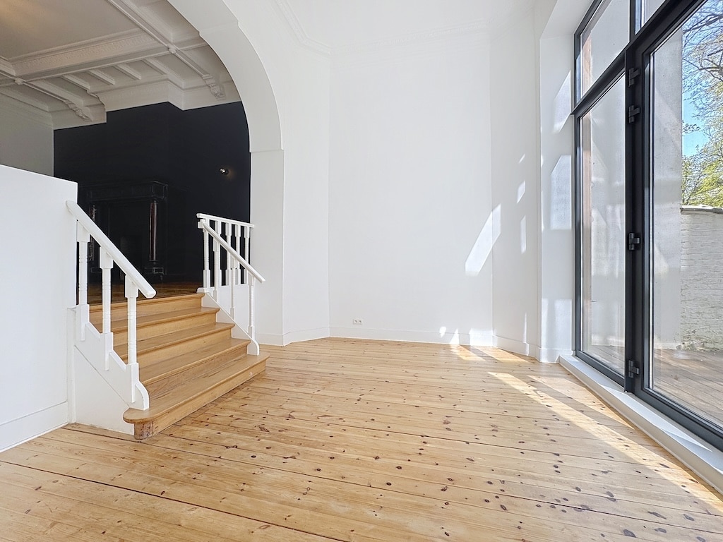 Intérieur élégant avec mur noir, escalier blanc, lumière naturelle et parquet en bois chaleureux.