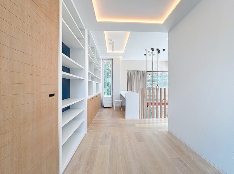 Salon moderne avec bibliothèque blanche, lumière naturelle et ambiance chaleureuse.
