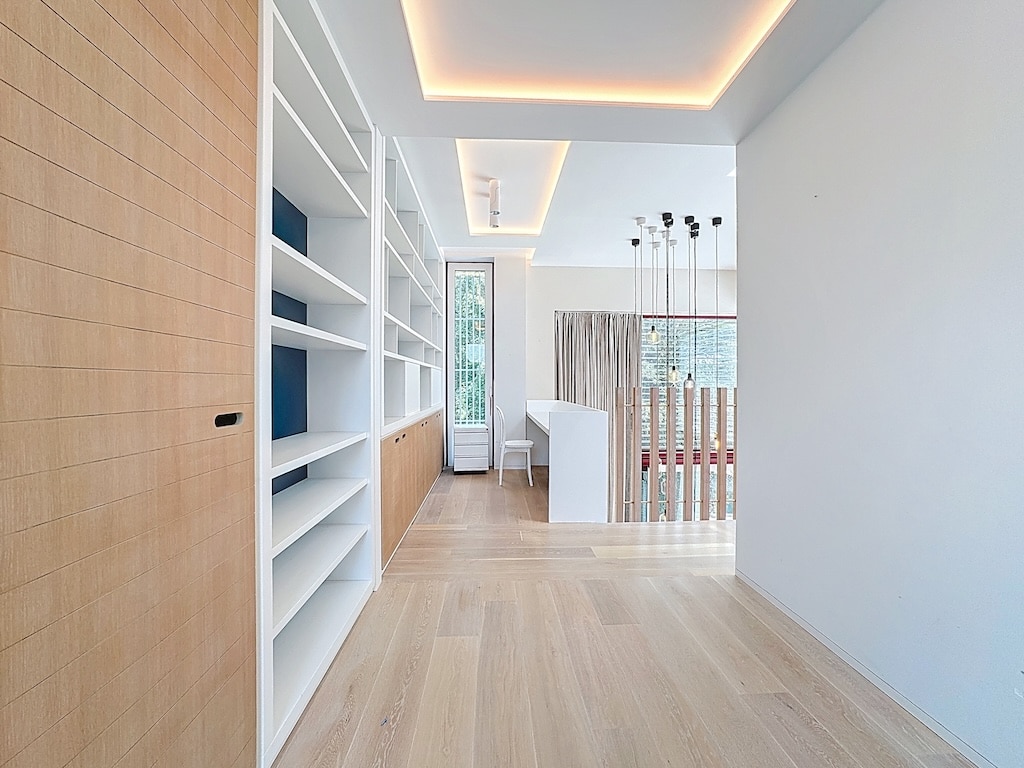 Salon moderne avec bibliothèque blanche, lumière naturelle et ambiance chaleureuse.