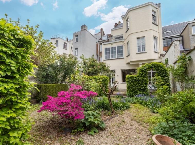 Jardin paisible avec maison élégante, fleurs colorées et ambiance sereine sous un ciel bleu.