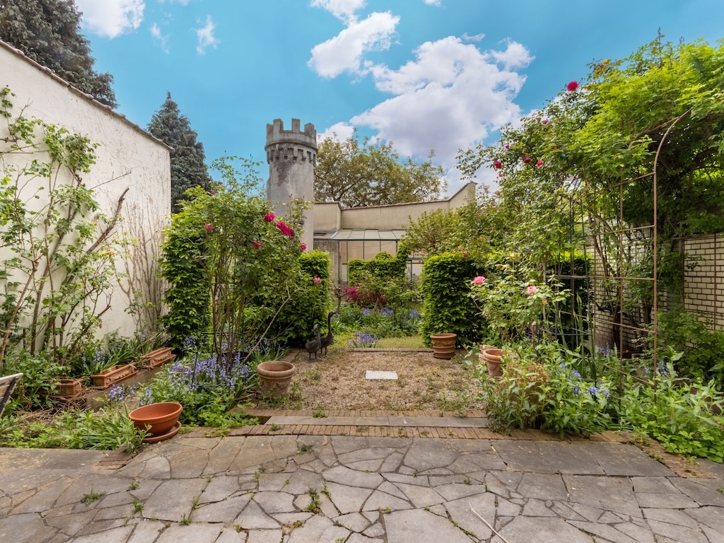 Jardin féerique avec tour, chemin pavé et fleurs colorées sous un ciel bleu.