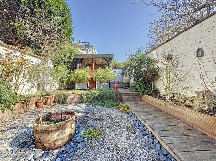 Jardin zen avec gazebo en bois, végétation abondante et ambiance paisible.
