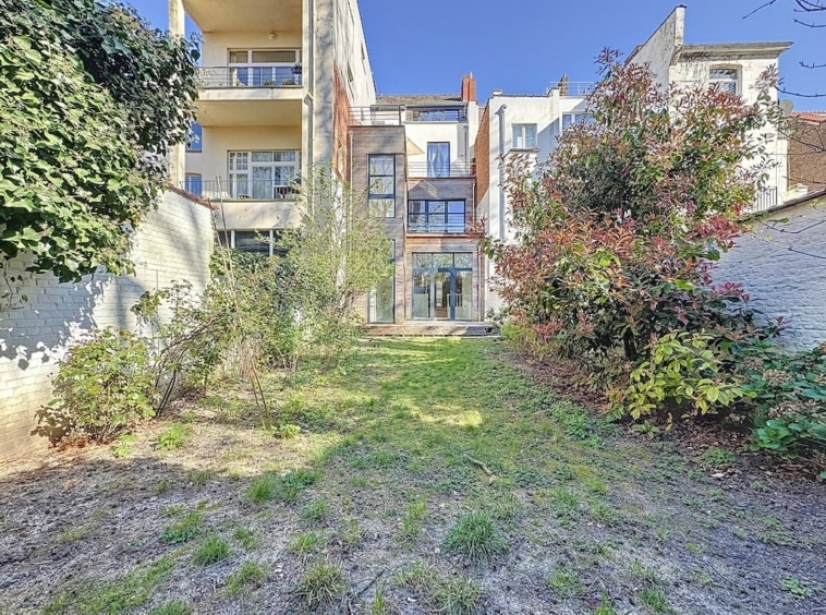 Jardin moderne paisible avec végétation luxuriante et vue sur résidence contemporaine ensoleillée.