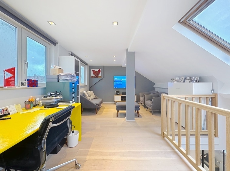 Loft lumineux avec espace de travail coloré, coin détente et mobilier moderne, idéal pour travailler et se relaxer.