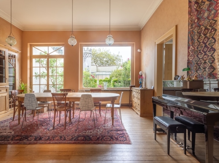 Salle à manger lumineuse avec table élégante, piano, vue jardin et décoration chaleureuse.