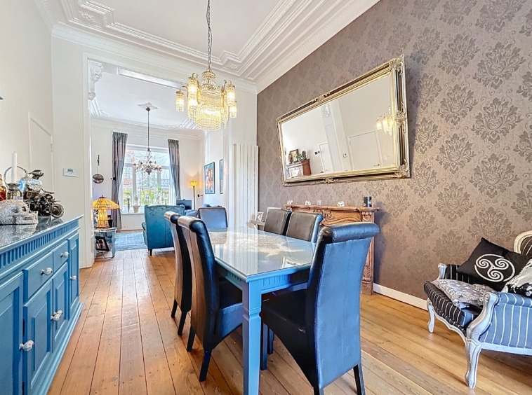 Salle à manger moderne élégante avec table en verre, miroir doré, buffet bleu, et coin détente.