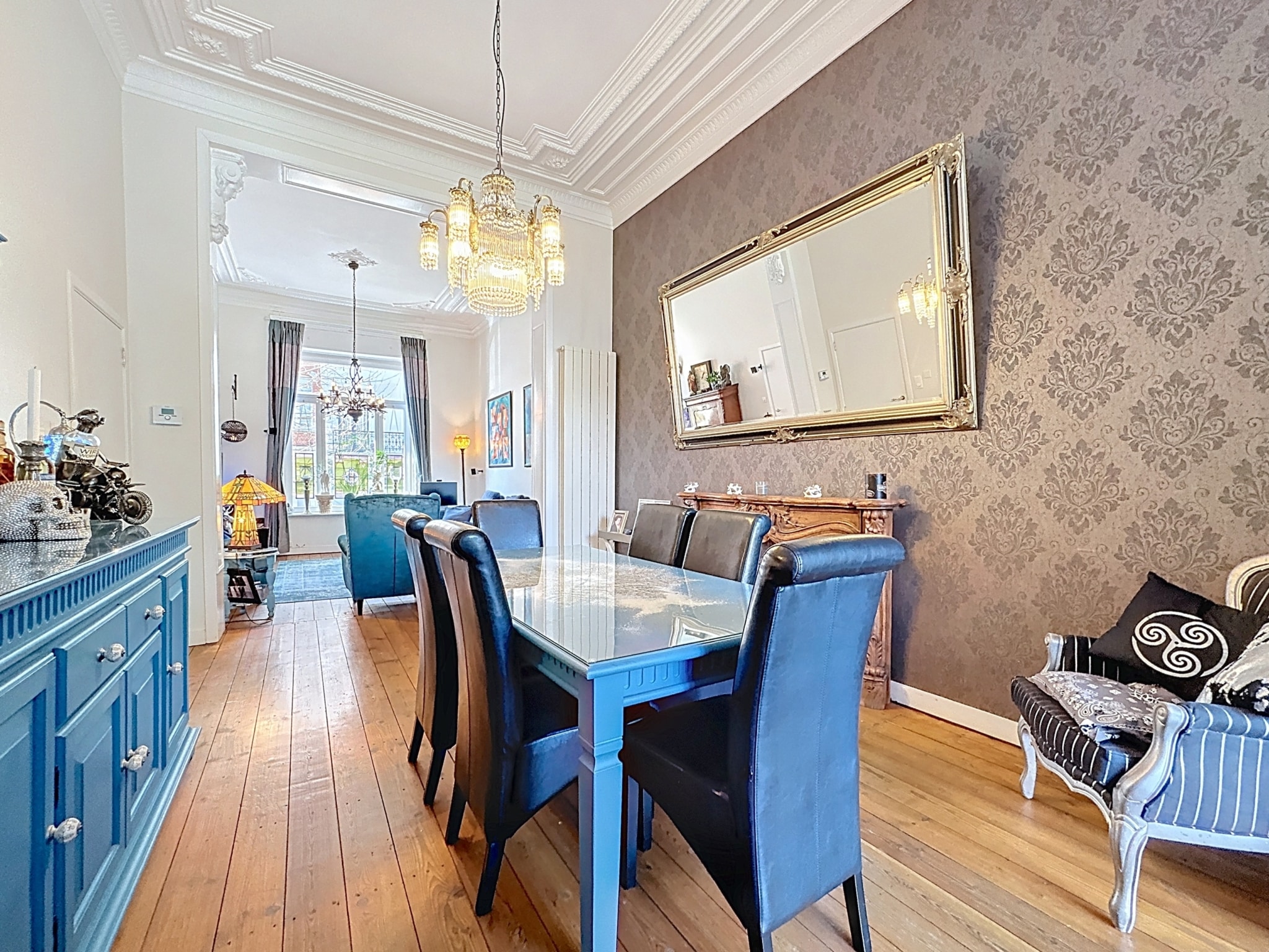 Salle à manger moderne élégante avec table en verre, miroir doré, buffet bleu, et coin détente.