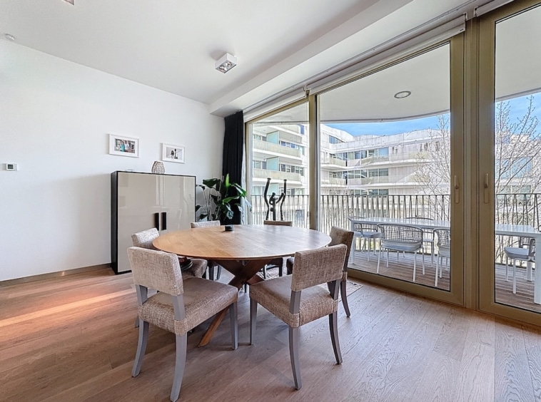 Salle à manger moderne lumineuse avec balcon, mobilier en bois, œuvres dart et plantes décoratives.