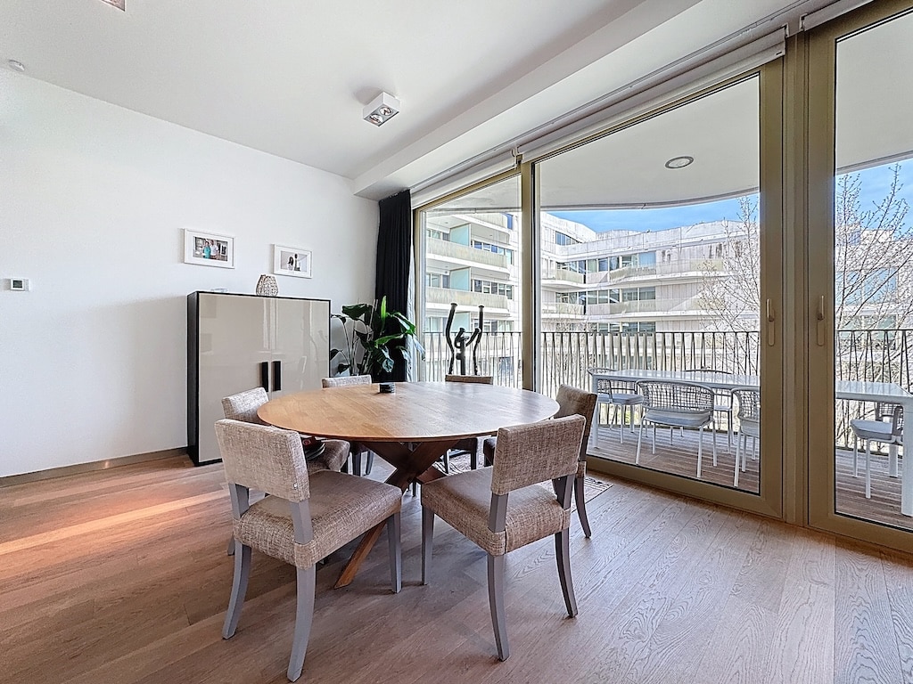 Salle à manger moderne lumineuse avec balcon, mobilier en bois, œuvres dart et plantes décoratives.