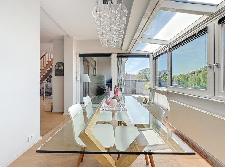 Salle à manger moderne lumineuse avec grandes fenêtres, mobilier élégant et vue panoramique extérieure.