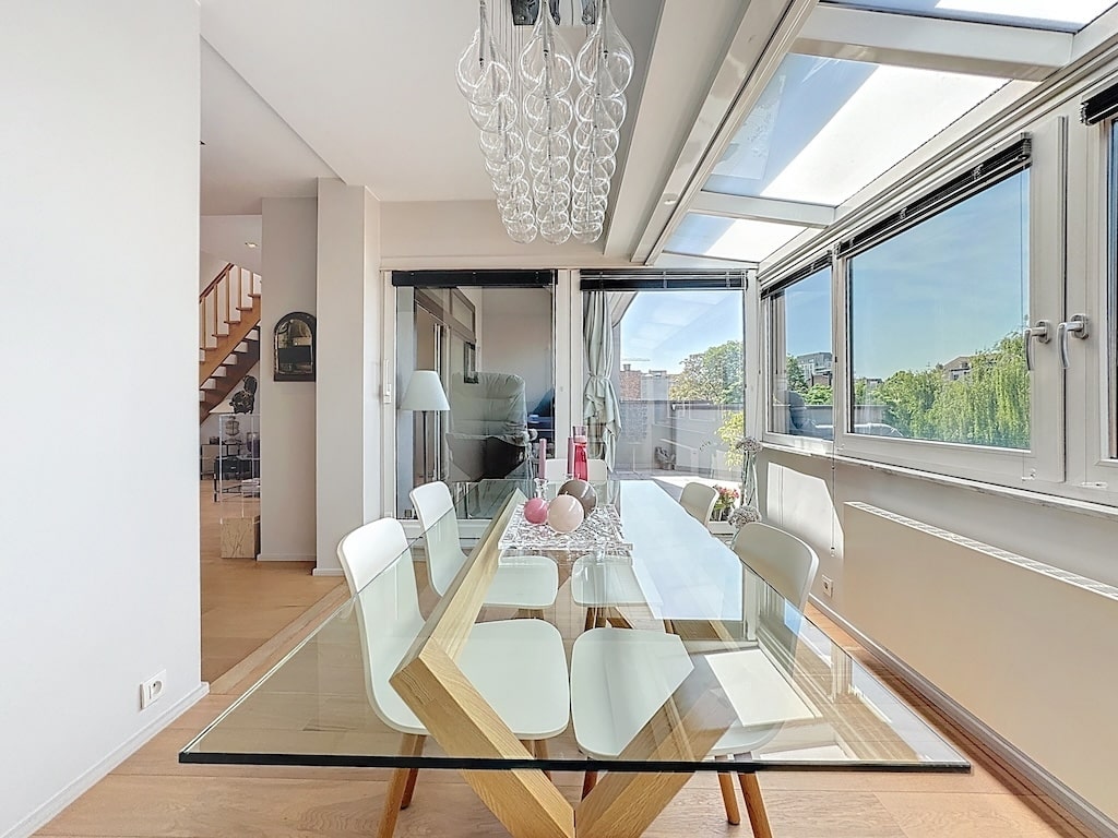 Salle à manger moderne lumineuse avec grandes fenêtres, mobilier élégant et vue panoramique extérieure.