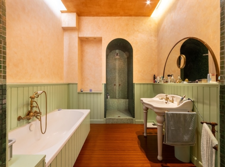 Salle de bain élégante avec baignoire vintage, mosaïque verte, murs peachy, ambiance chaleureuse et raffinée.