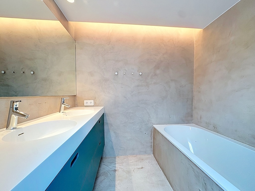 Salle de bain moderne minimaliste avec vanity teal, baignoire intégrée et éclairage doux.